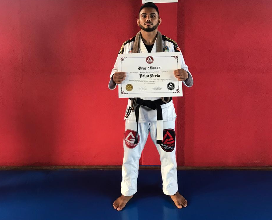 jovem de quimono em pé posando para a foto e mostrando certificado de faixa preta